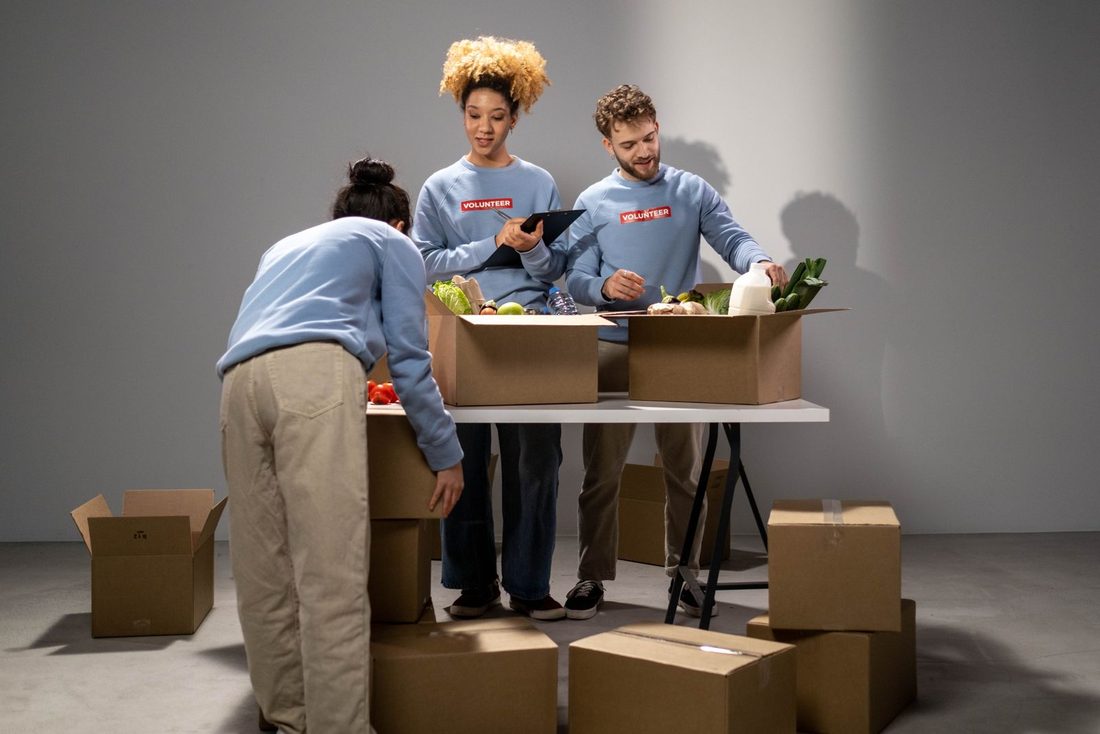 Three volunteers pack donated food into cardboard boxes at a distribution table